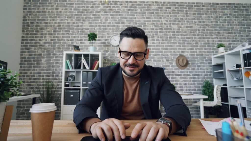 A man in glasses is sitting at a desk with a laptop