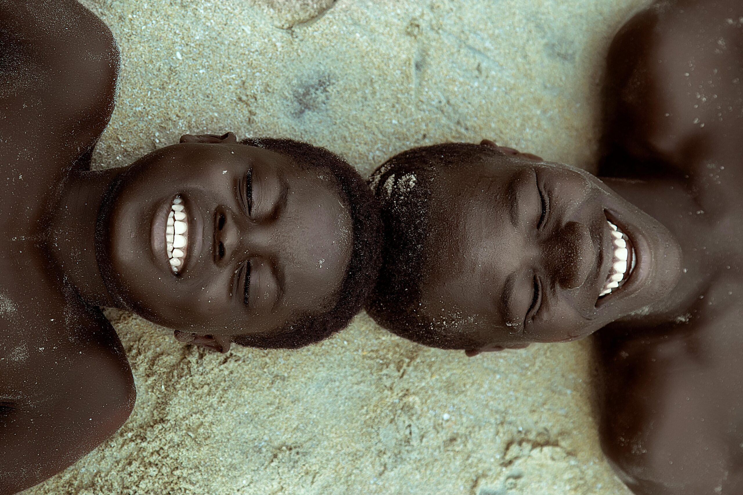 Two smiling African boys lying on the sandy beach in Ghana, expressing joy and togetherness.