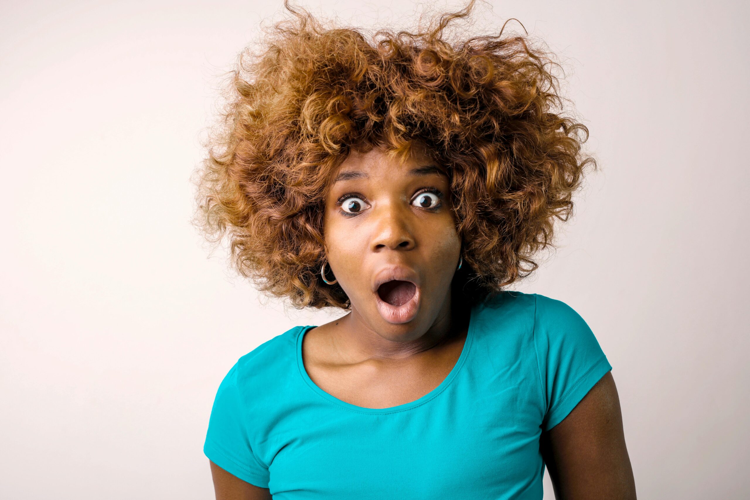 Portrait of a surprised woman with curly hair in a teal top on a white background.