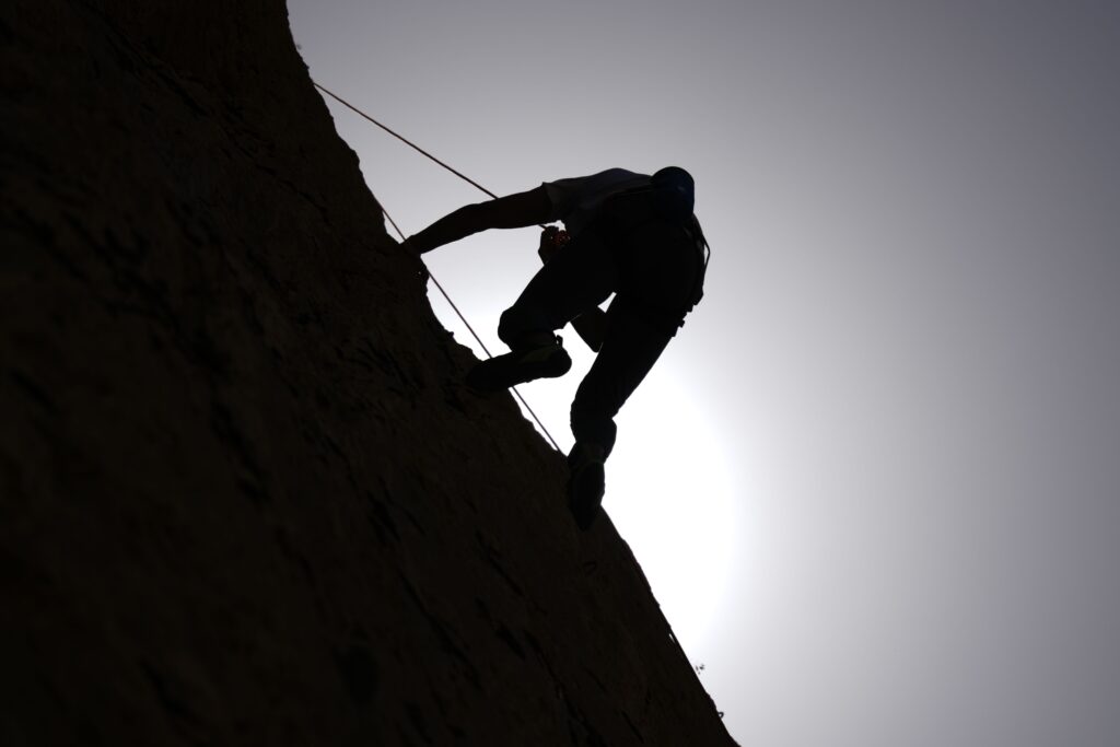 Dramatic silhouette of a rock climber scaling a cliff under a bright sun.