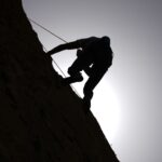 Dramatic silhouette of a rock climber scaling a cliff under a bright sun.