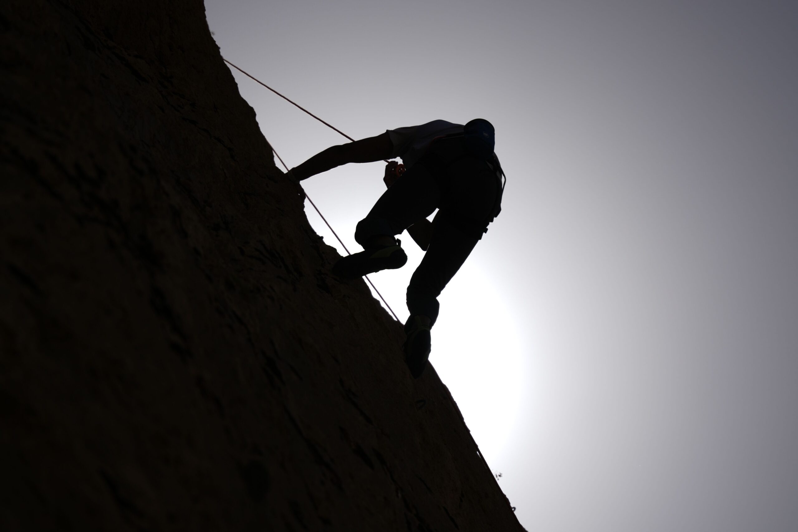 Dramatic silhouette of a rock climber scaling a cliff under a bright sun.