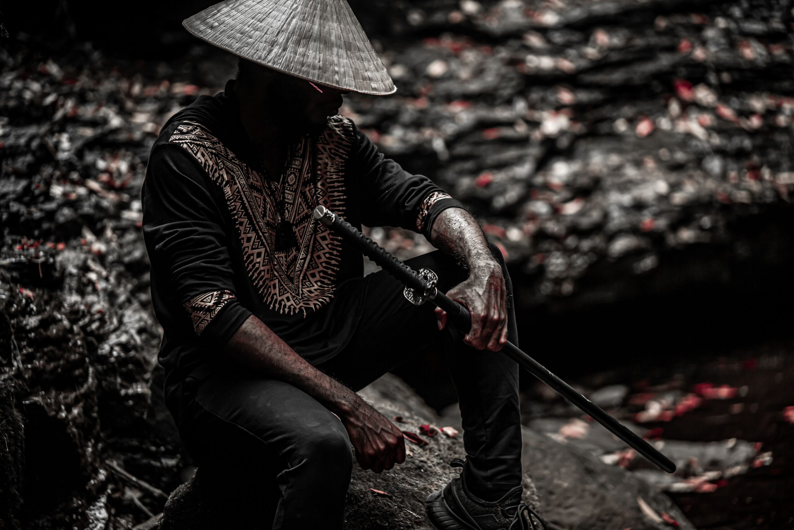 A dramatic outdoor portrait of a man holding a samurai sword, wearing traditional attire with a hat.