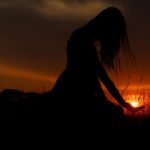 Artistic silhouette of a woman at sunset, capturing a tranquil moment in a grassy field.