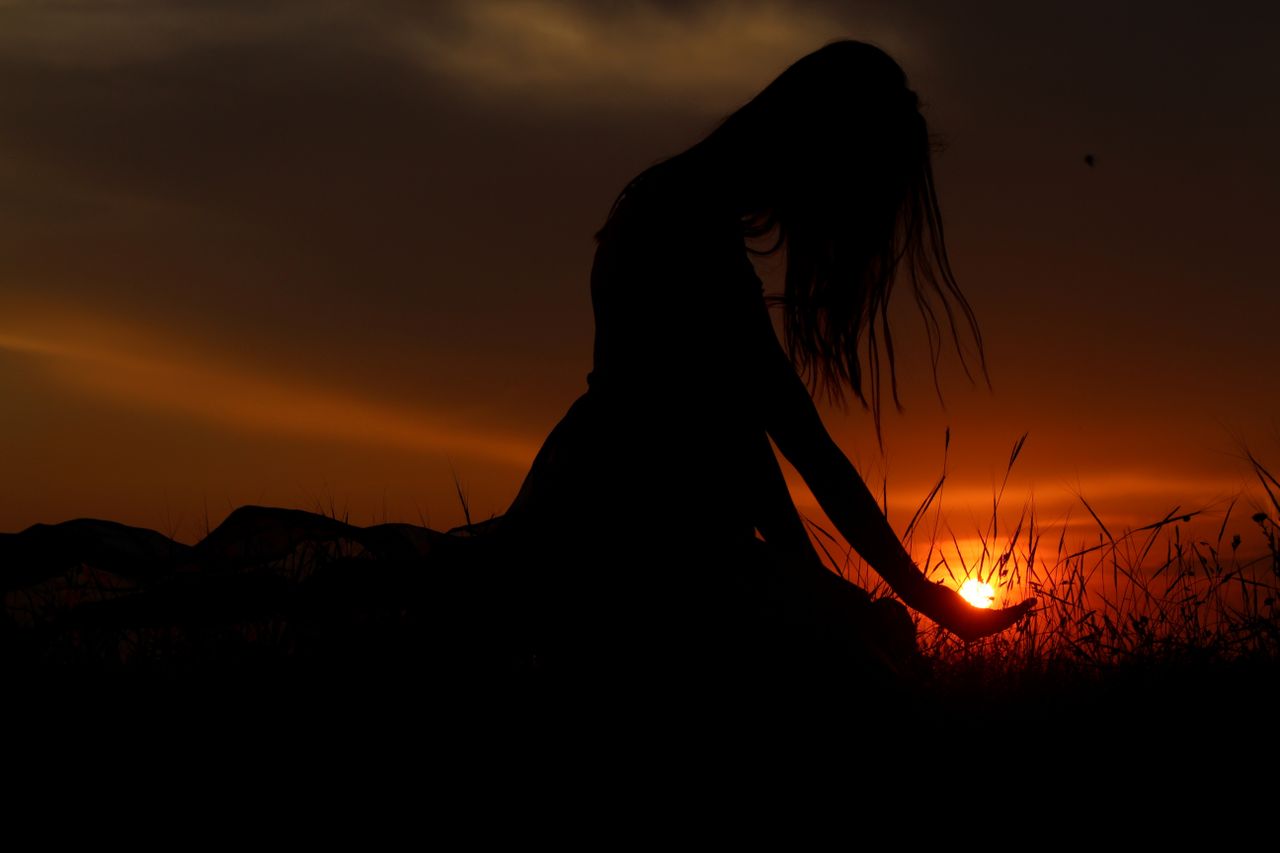 Artistic silhouette of a woman at sunset, capturing a tranquil moment in a grassy field.